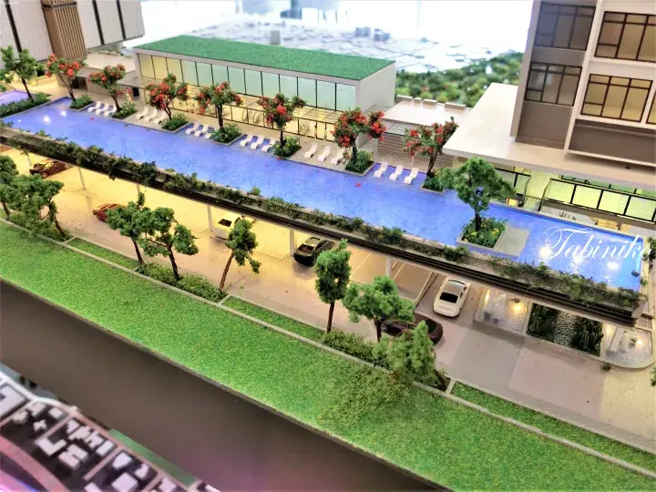 Architectural model showing a modern residential complex with a rooftop infinity pool, landscaped gardens, and parking area.
