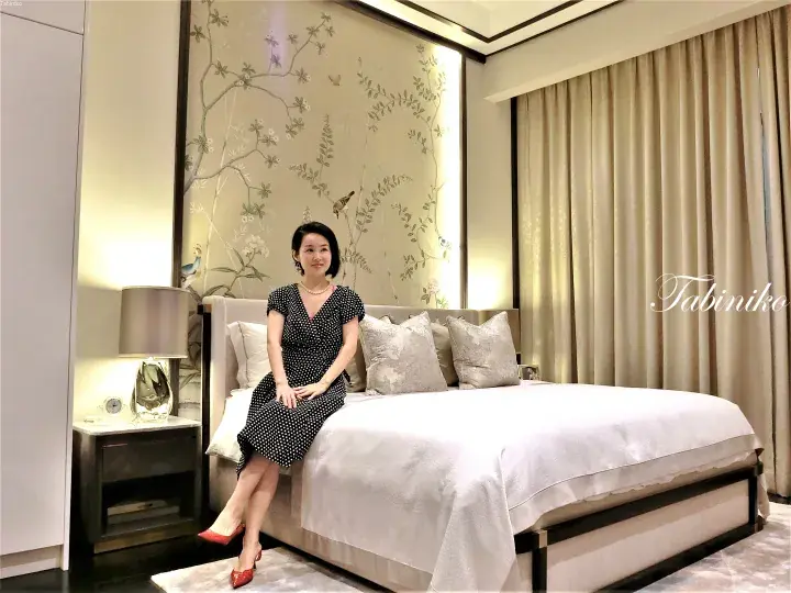 Woman in polka dot dress sitting on a bed in a luxury hotel room with floral wallpaper and modern decor.
