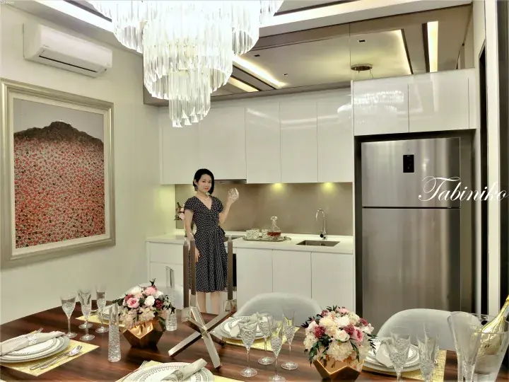 Woman in polka-dot dress in a modern kitchen with a large crystal chandelier and dining table set for a party.