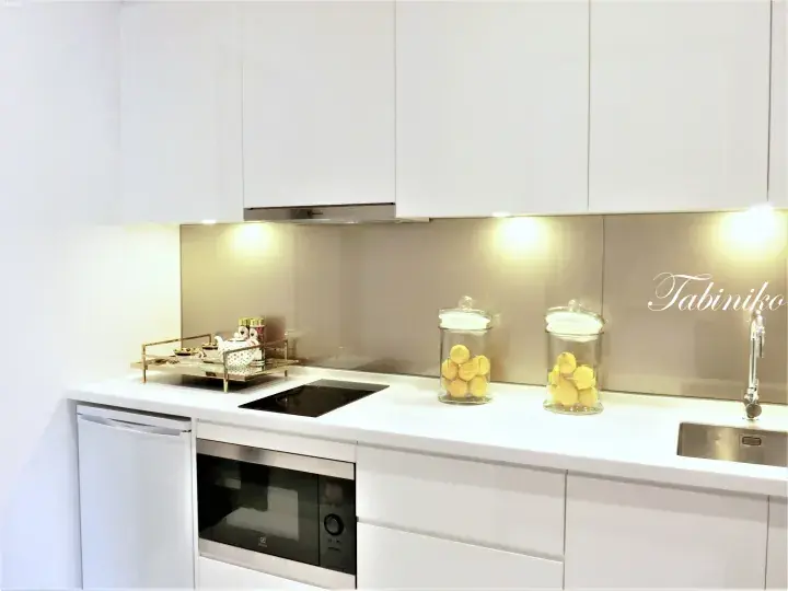 Modern white kitchen with sleek cabinets, built-in oven, induction cooktop, and decorative lemon jars on the countertop.