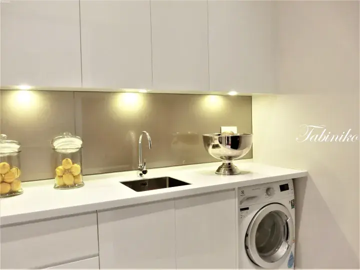 Modern white kitchen with a sink, glass jars of lemons, and an integrated washing machine.