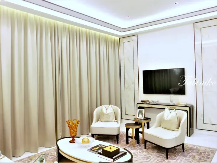 Luxury living room with cream armchairs, marble wall panels, and a flat-screen TV in a modern Malaysian property.