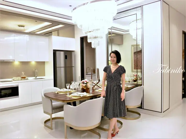 Woman in polka-dot dress standing in modern dining area with white kitchen and crystal chandelier