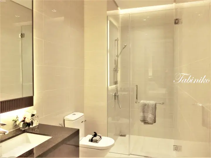 Modern hotel bathroom featuring a glass shower enclosure, dark stone vanity, and beige tiled walls.