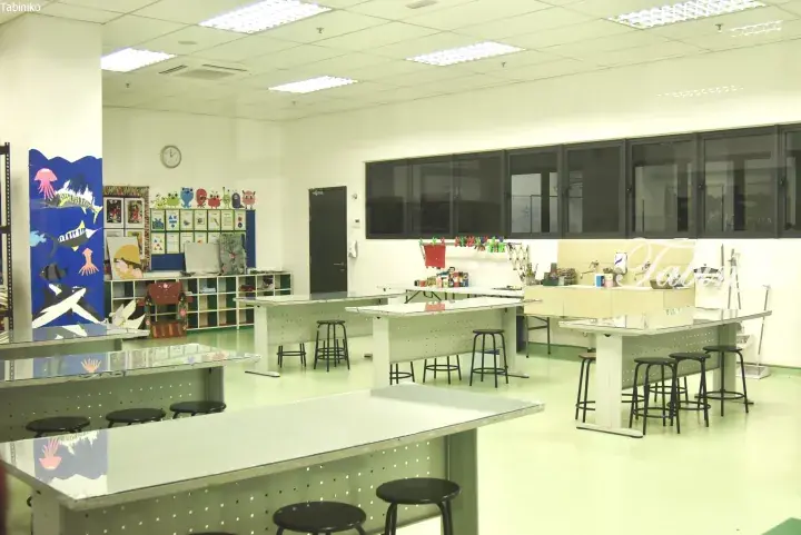 Bright, modern classroom with white tables, black stools, and colorful student artwork displayed on walls and shelves.