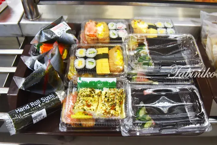 Assorted packaged sushi including hand rolls and sushi boxes displayed on a supermarket shelf.