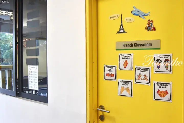 Yellow French classroom door with Eiffel Tower and hand gesture posters.