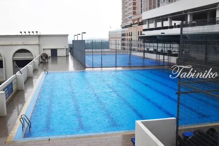 Outdoor swimming pool and tennis court on a rooftop terrace with surrounding high-rise buildings.
