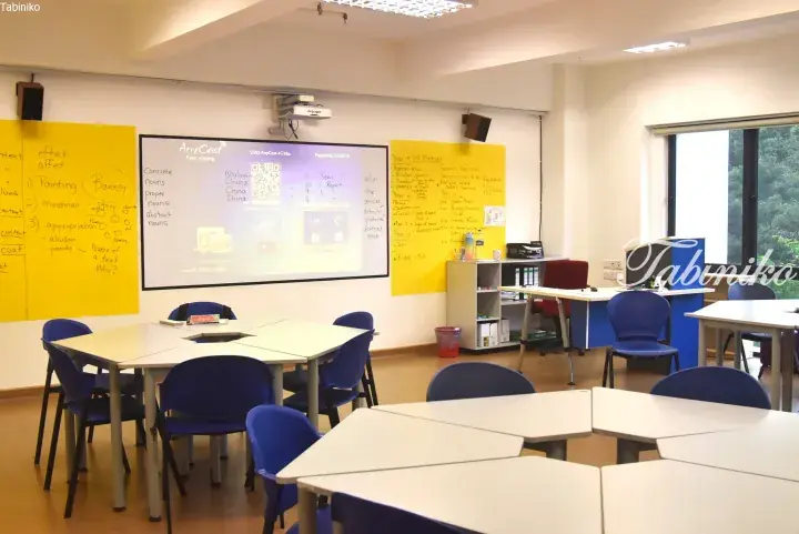 Modern classroom with whiteboards, projector screen, and blue chairs arranged for collaborative learning.