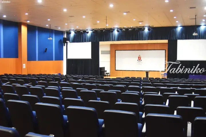 Spacious auditorium at Peninsula International School Australia with rows of blue seats and a stage featuring the school crest.