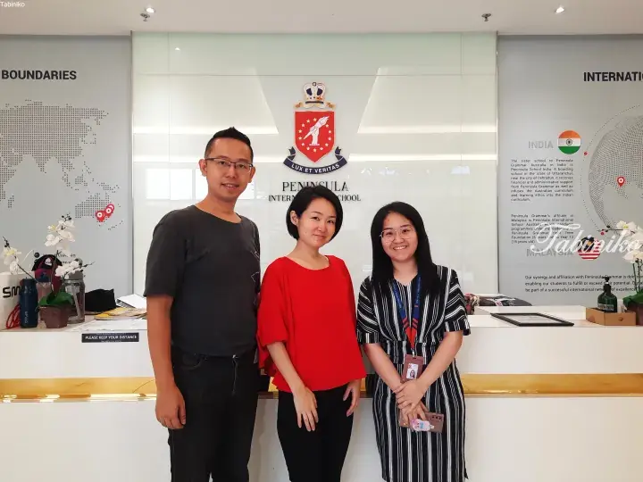 Three people standing in front of the Peninsula International School Malaysia reception desk.