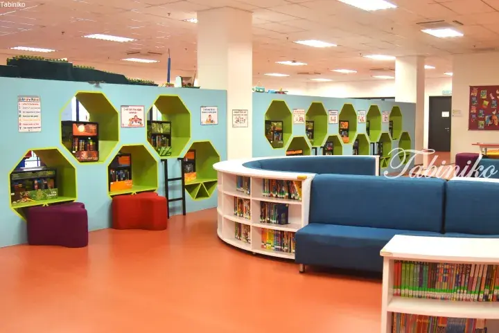 Colorful children’s library interior with hexagonal green shelves, blue sofa, and orange flooring
