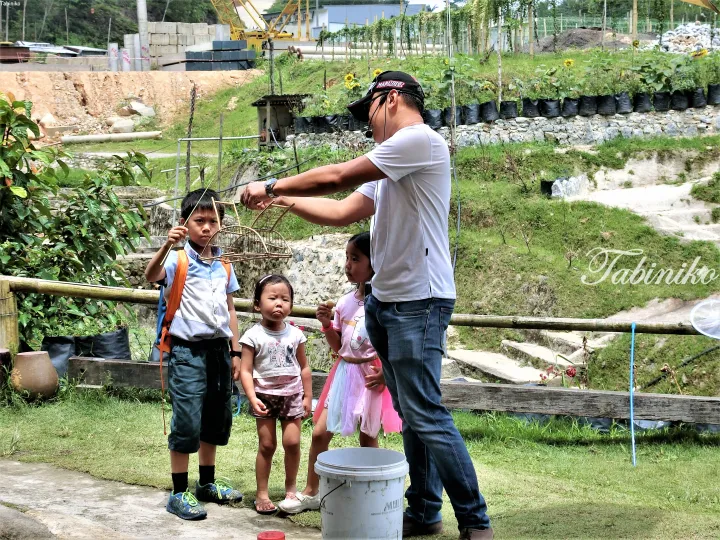 Guide shows children a handmade bamboo birdcage at a Malaysian eco-park with construction in the background
