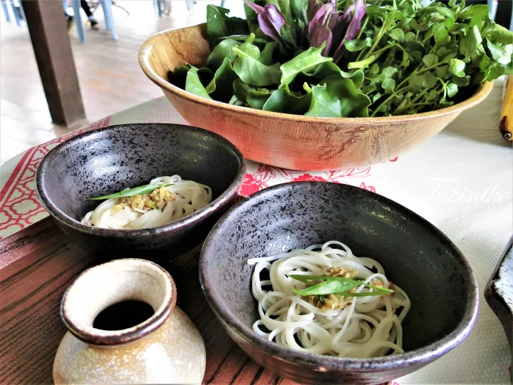 Two bowls of white noodles with garlic and green onions served alongside a wooden bowl of fresh mixed greens.