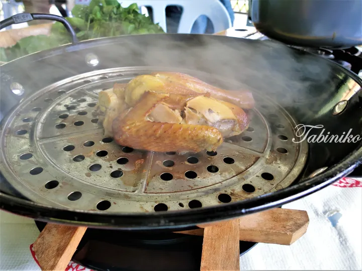 Steaming chicken pieces on a metal rack inside a wok, with fresh herbs in the background.