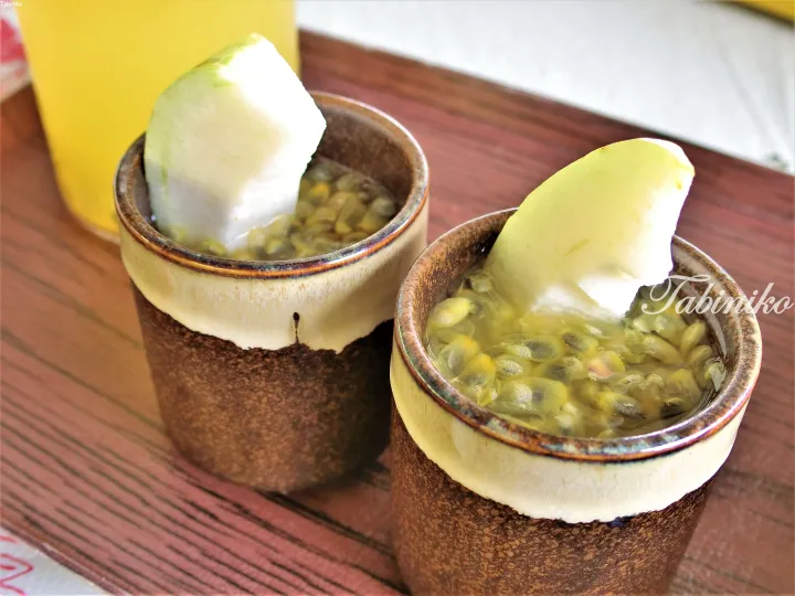 Two ceramic cups filled with passion fruit pulp and topped with fresh fruit slices on a wooden table.