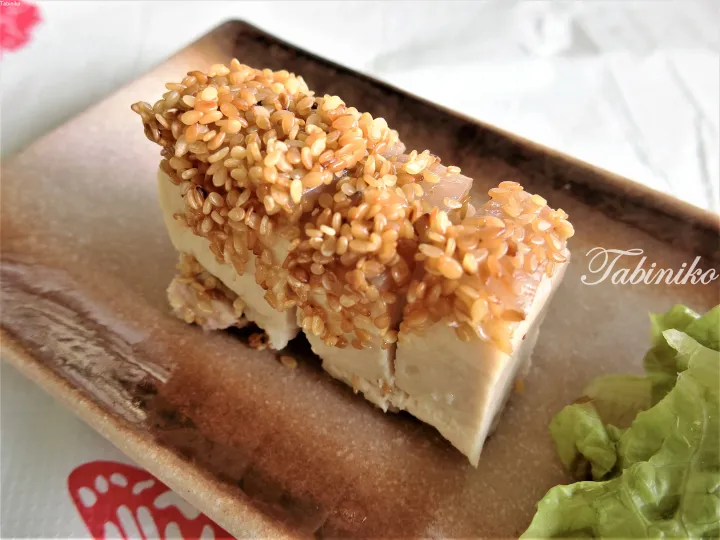 Slices of tofu topped with toasted sesame seeds served on a rustic ceramic plate with lettuce.