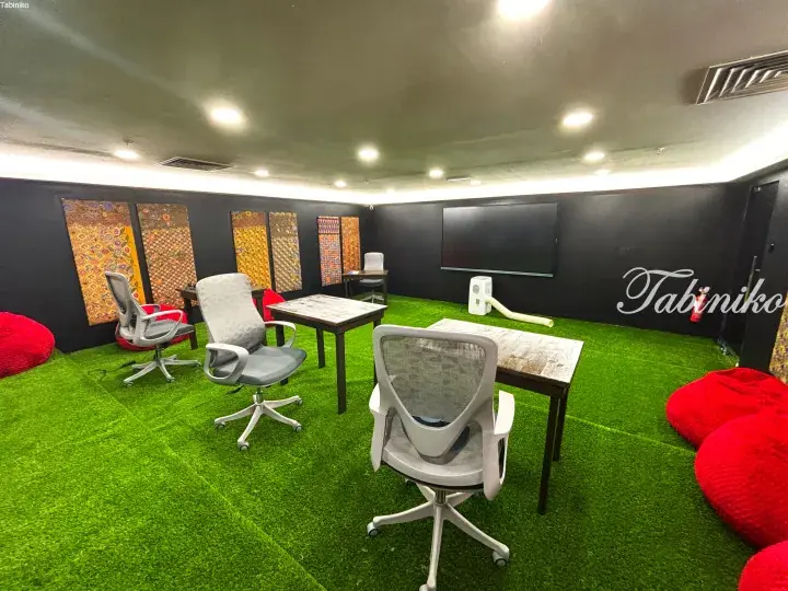 Modern coworking space with green artificial grass flooring, grey office chairs, wooden desks, and colorful wall art.