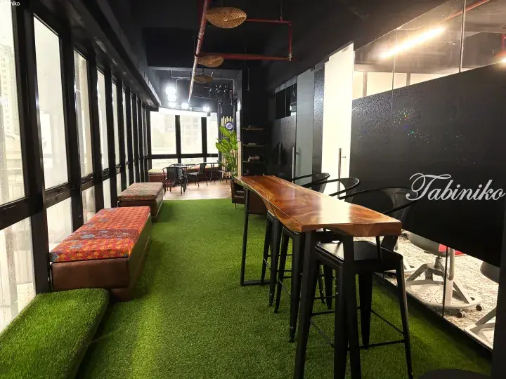 Modern co-working space with green artificial turf, wooden bar table, and cushioned benches near large windows