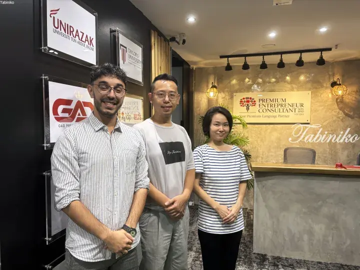 Three people standing in front of a reception desk with signs for Unirazak, Taylor’s University, and Premium Entrepreneur Consultant.