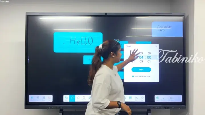 Teacher setting a timer on a smartboard during an English vocabulary lesson in a modern classroom.