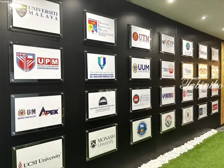 Wall displaying logos of Malaysian universities including UM, UPM, and Monash University.