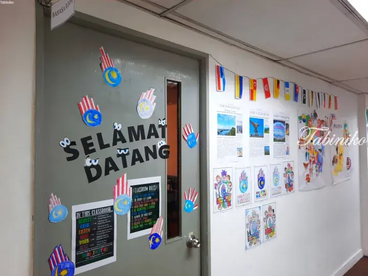 Malaysian classroom door decorated with handprints and ‘Selamat Datang’ sign, alongside wall displays of student art and national flags.
