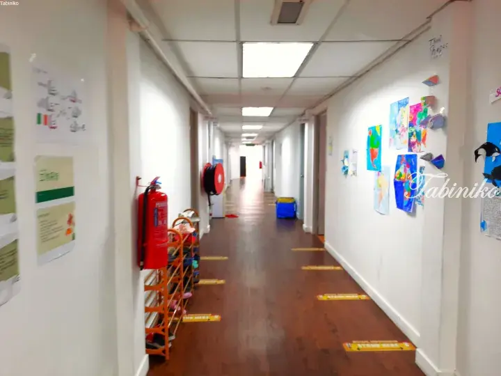 A hallway in a Malaysian school or daycare with children’s artwork on the walls, a fire extinguisher, and social distancing floor markers.