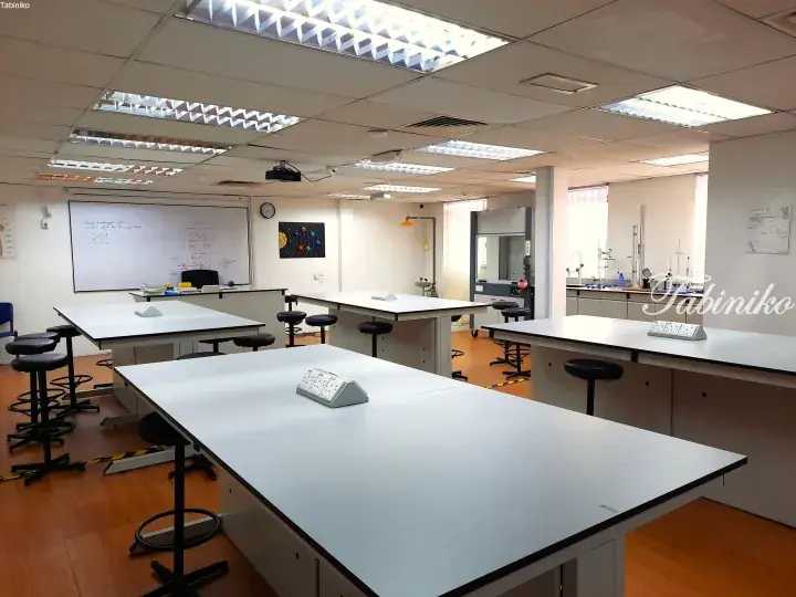 Modern science classroom with white lab tables, stools, whiteboard, and solar system poster.