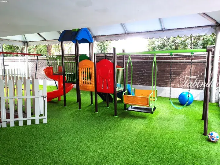 Colorful playground with slide and swings on artificial grass under a shelter, suitable for children.