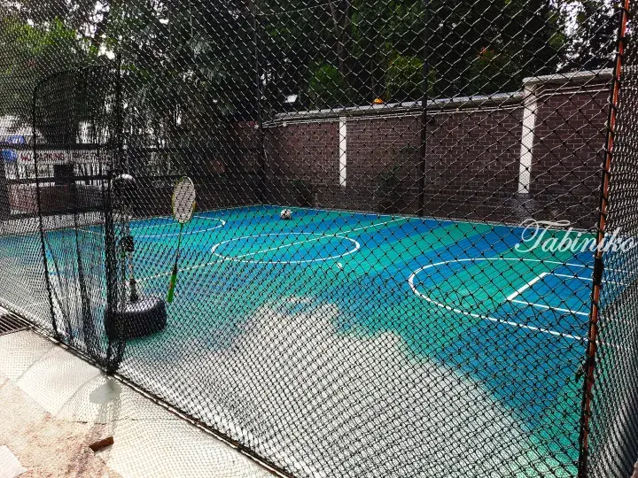 View of a blue and green badminton court enclosed by a black safety net, with a racket and shuttlecock visible inside.