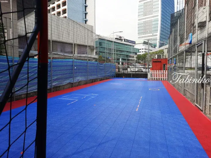 Blue and red modular sports court with basketball hoops in a high-rise urban setting in Kuala Lumpur.