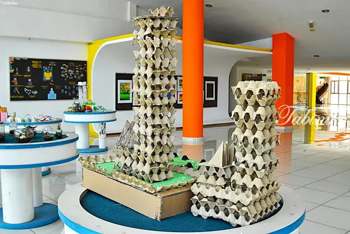 Creative student project using egg cartons to build tall tower structures in a bright school exhibition hall.