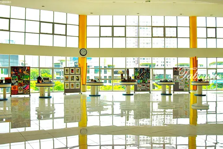 Bright school lobby with large windows, yellow pillars, and student art displays on white tiled floors.