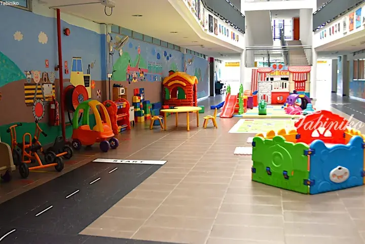 Colorful indoor playground with ride-on toys, playhouses, and a painted road in a Malaysian property common area.