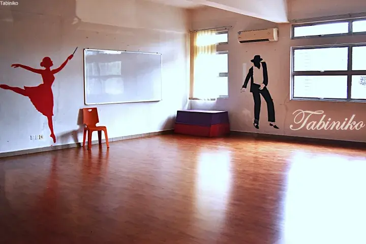Bright dance studio with wooden floors, wall decals of dancers, and a whiteboard.
