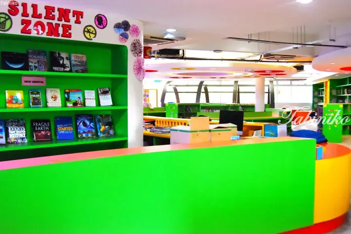 Colorful library interior with green shelves, a ‘Silent Zone’ sign, and a curved reception desk.