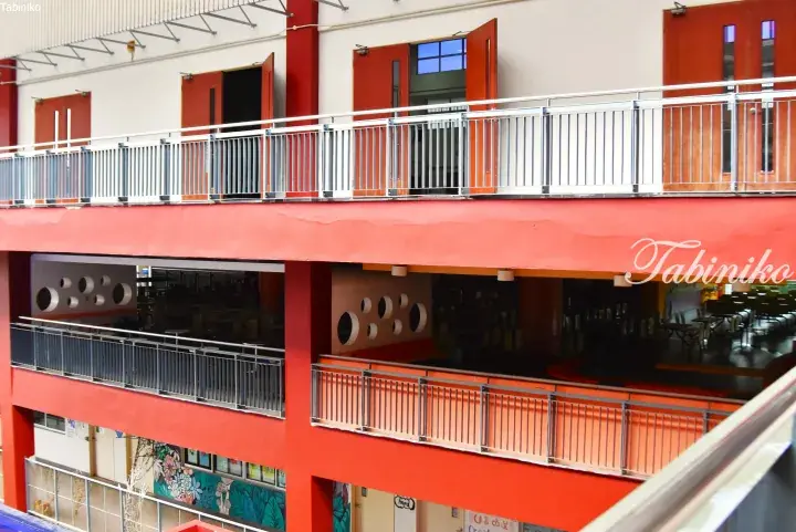 Modern building interior with bright red beams, white railings, and circular wall cutouts in a multi-level atrium.