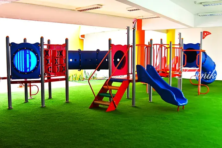 Colorful indoor playground with slides and climbing structures on green artificial turf for children’s recreation.