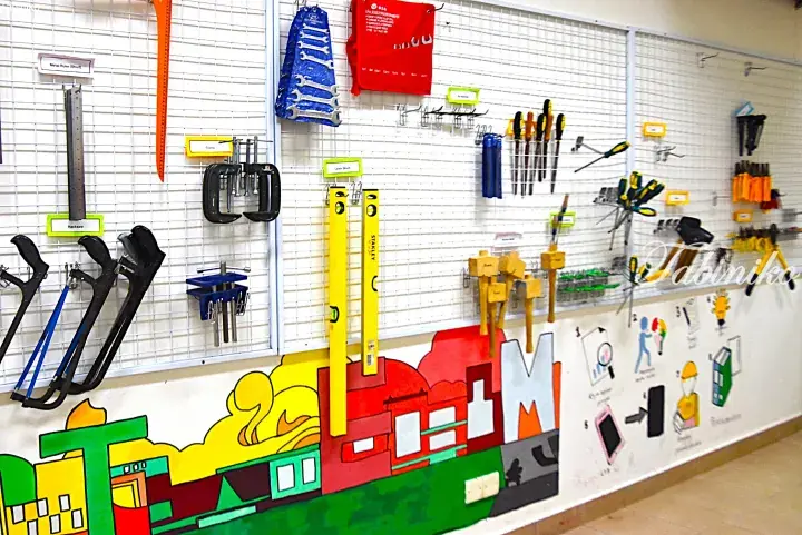 Organized workshop wall with labeled tools like hacksaws and levels above a colorful factory mural.