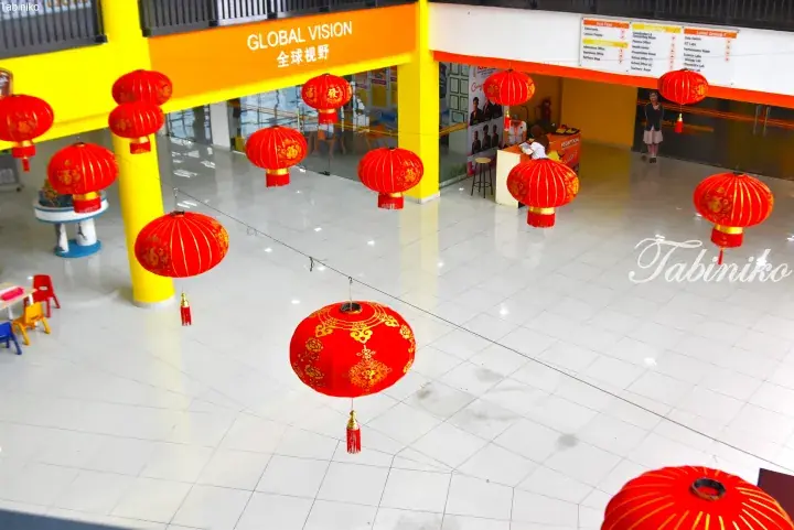 Red lanterns hang in a bright school lobby with yellow pillars and a Global Vision sign.