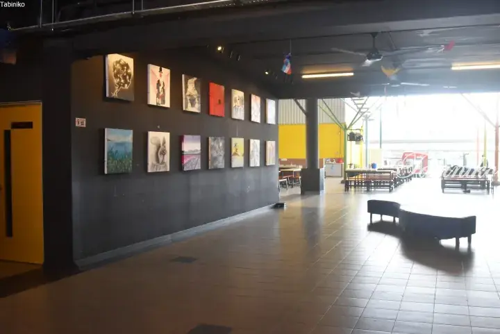 Gallery wall displaying various paintings in a spacious indoor area with tiled floors and seating.