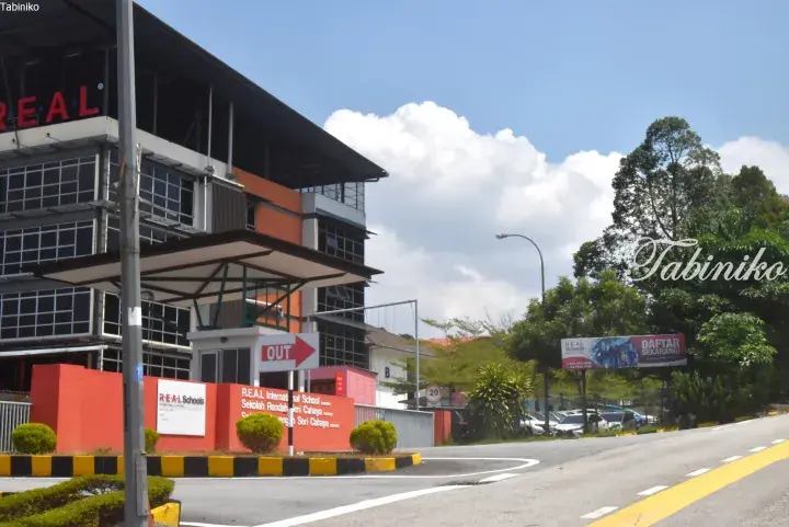 R.E.A.L International School entrance with orange walls, signage, and a modern building under a blue sky.