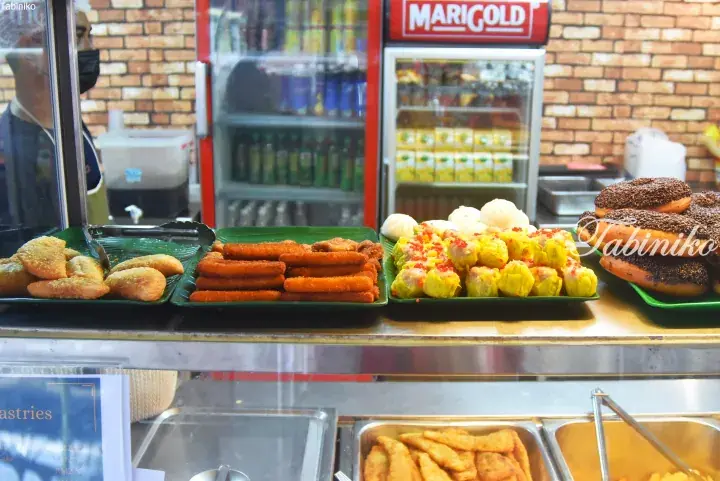 Assorted Malaysian breakfast items including fried pastries, fish sticks, siu mai, and chocolate donuts displayed at a food stall.