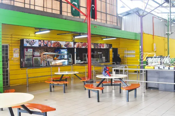 Colorful indoor food court with yellow walls, orange benches, and flags hanging from the ceiling.