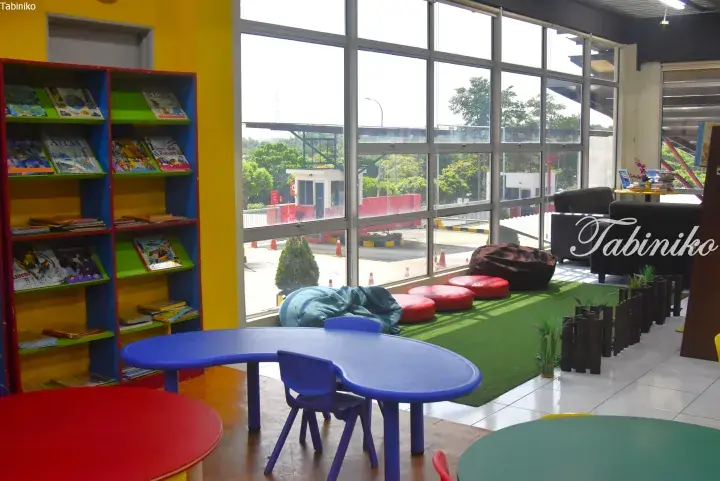 Colorful children’s reading area with bookshelves, bean bags, and large windows overlooking a green landscape.