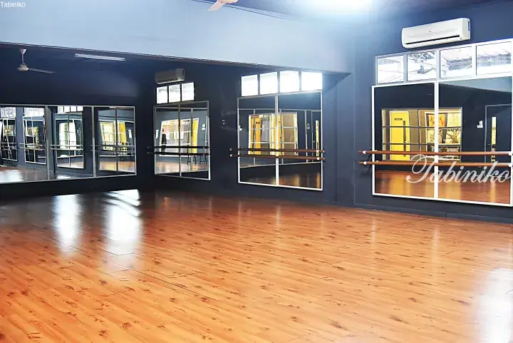 Spacious dance studio with polished wooden floors, wall mirrors, and ballet barres in a modern facility.