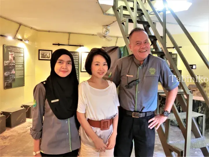 Guest posing with two staff members in grey uniforms at the entrance of Belum Rainforest Resort Malaysia.