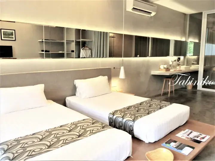 Modern hotel room with twin beds, concrete walls, and a vanity area.