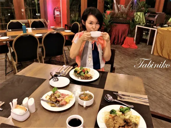 Woman enjoying a meal at a restaurant table with plates of food and drinks in a cozy dining setting.